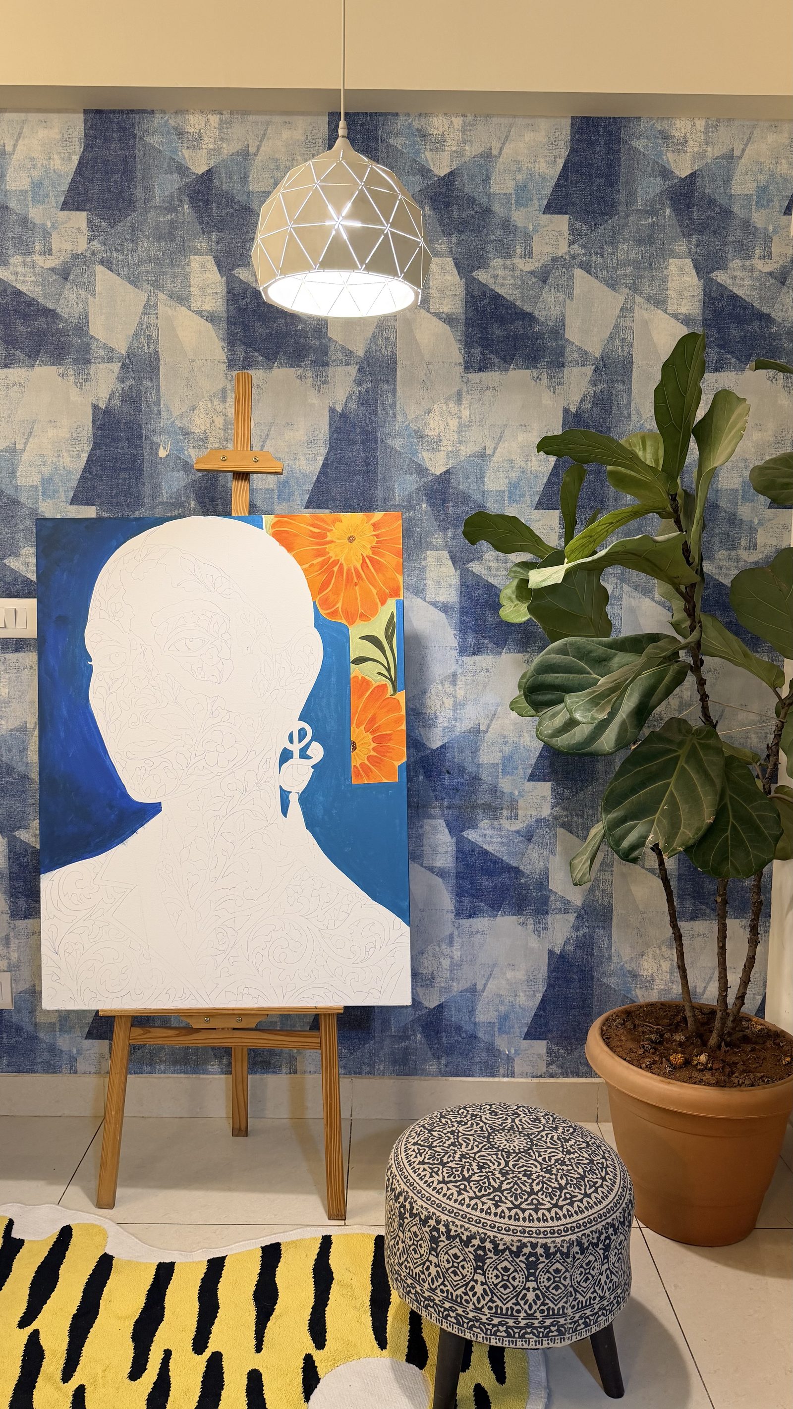 Unfinished painting on an easel in the pinkchutney studio, surrounded by blue geometric wallpaper and a fiddle-leaf fig